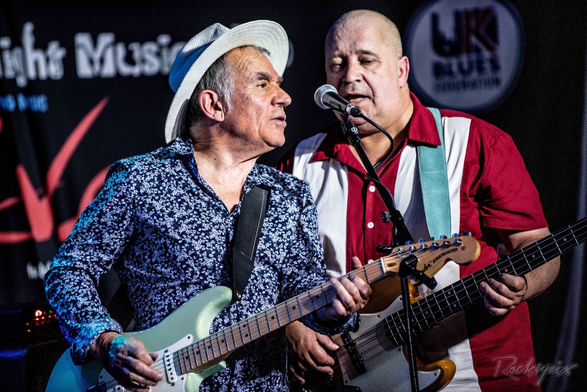 Robin Bibi singing at the microphone next to his bassist at a UK Blues Federation show