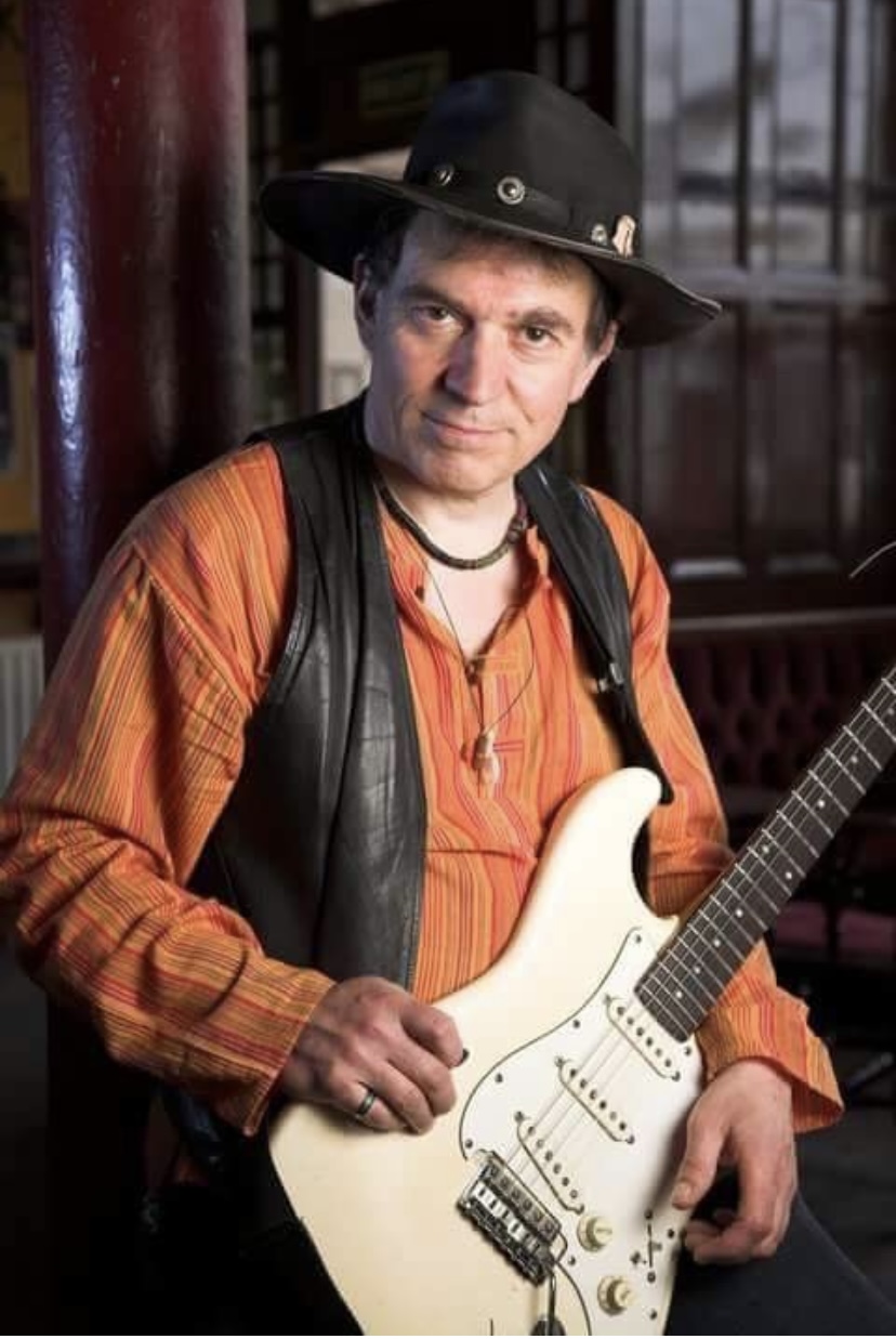 Portrait of Robin Bibi in a black hat and orange shirt holding a cream Stratocaster